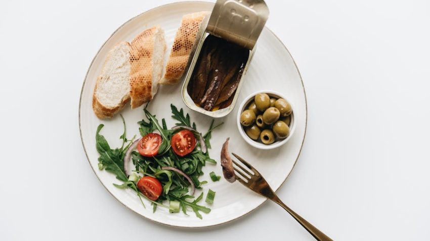 A gourmet Mediterranean dish featuring anchovies, olives, bread, and fresh salad on a plate.