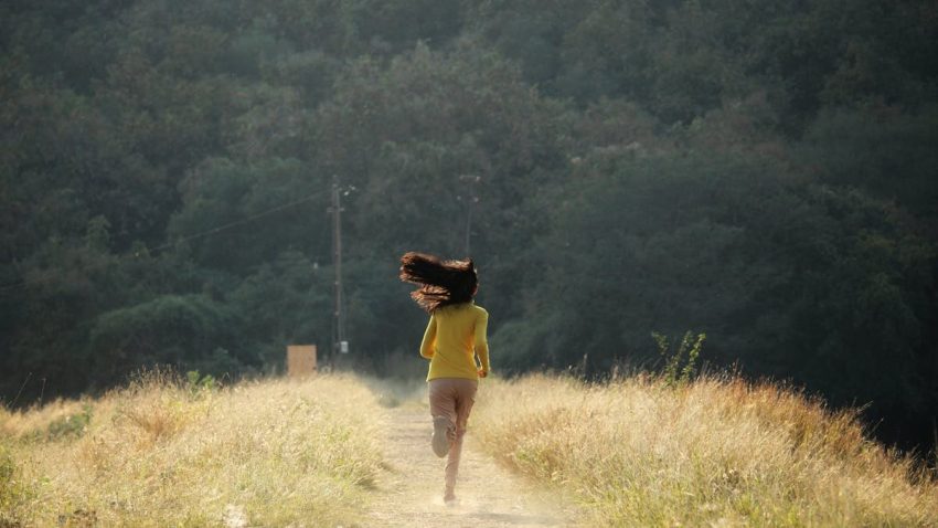 Young woman with long hair runs down a scenic path in summer. Embracing freedom and nature.